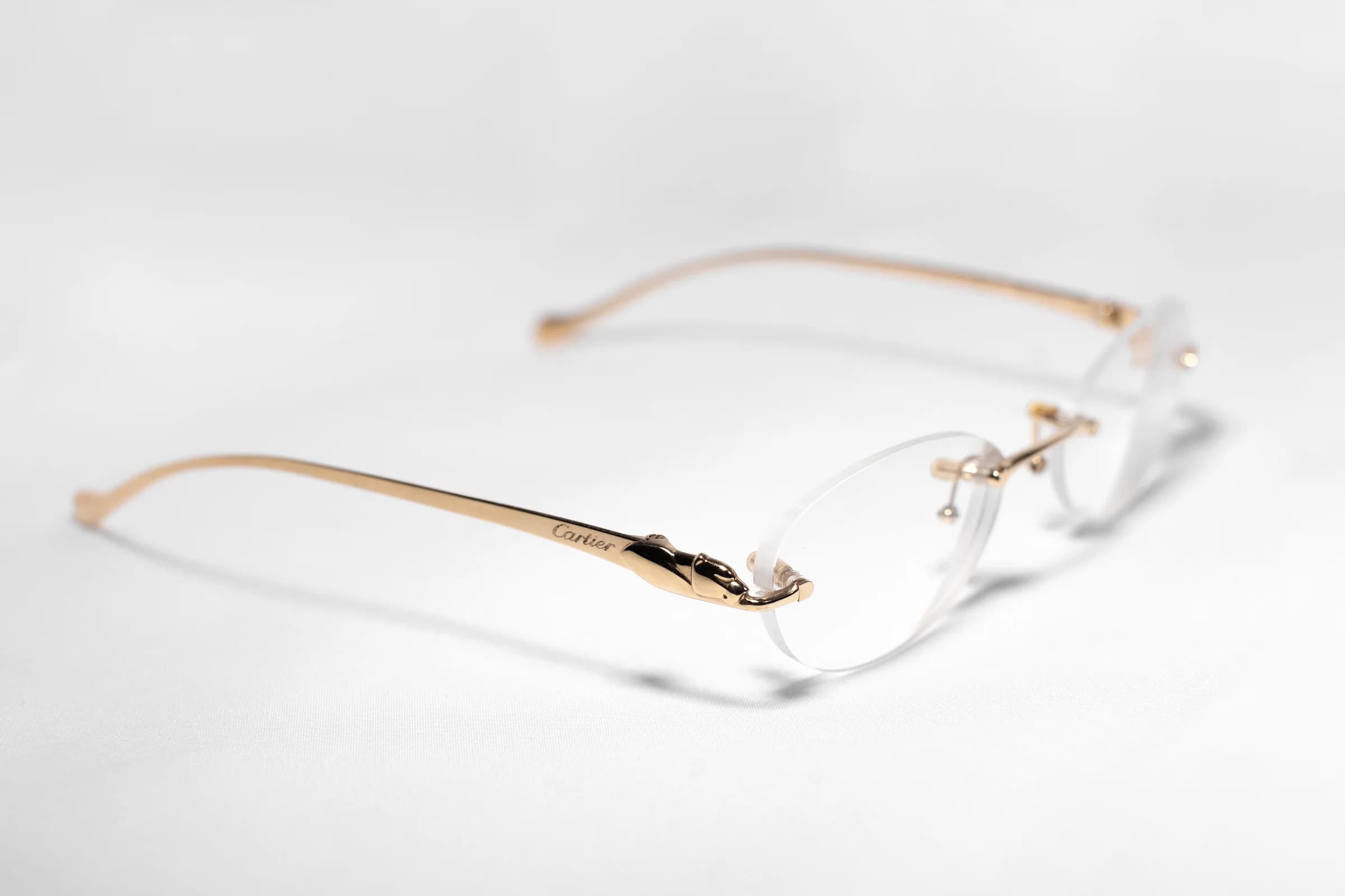 A gold rimless Cartier frame on a white surface, the panther detail on the temple in focus.